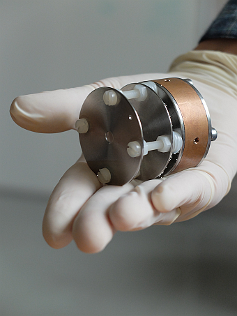 Photo of a single cavity ECR source module with two aperture electrodes, presented on a gloved hand palm