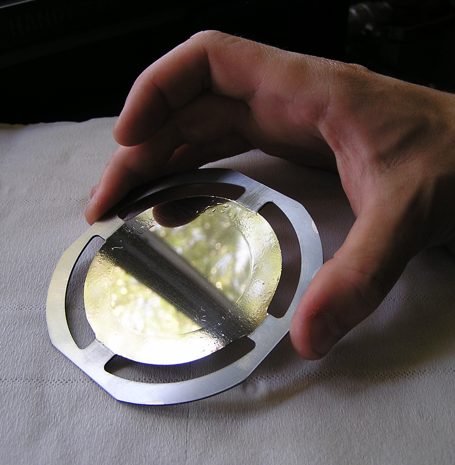 Photo of bare hands holding a Ø100mm Mylar® foil on a metallic holder, with a deposit realized by multi beam sputtering
