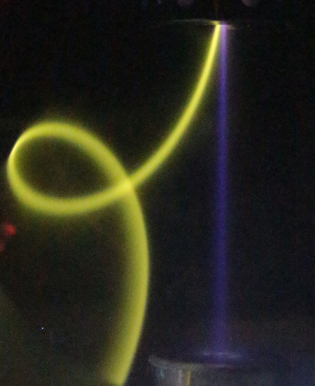 Photo of the TES ion source facing a Faraday cup, showing a blue parallel beam of negative oxygen ions, and a curly yellow beam of magnetically deflected electrons